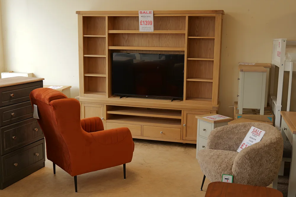 A large wood-finish TV and storage unit with an orange armchair and a pale textured chair